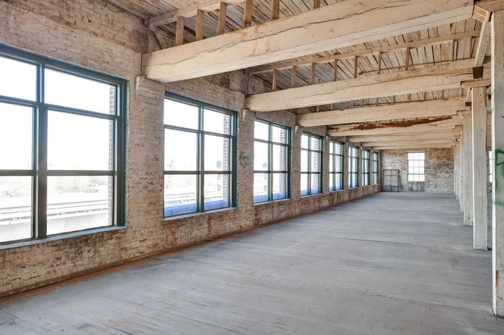 Sunlit upper floor of the restored warehouse with original timber beams and steel windows